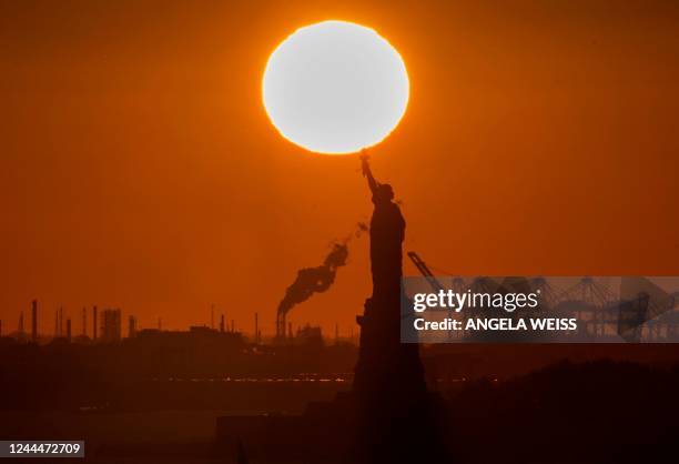 The sun sets behind the Statue of Liberty in New York on November 3, 2022.