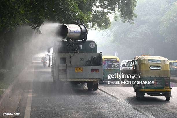 Commuters ride past an anti-smog gun spraying water to curb air pollution amid heavy smog conditions in New Delhi on November 4, 2022.