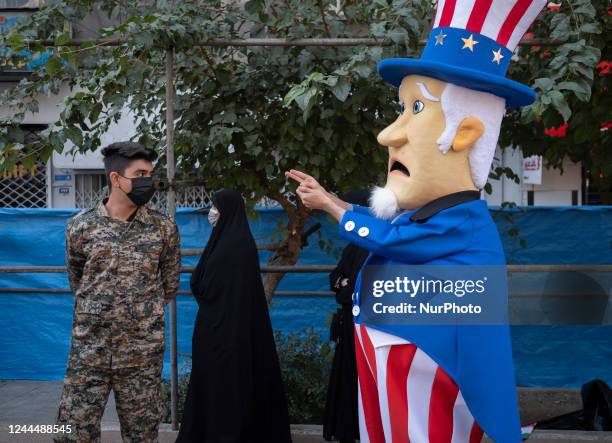 Member of the Basij paramilitary force looks at a man dressed as Uncle Sam performing during a gathering out of the former U.S. Embassy in Tehran to...