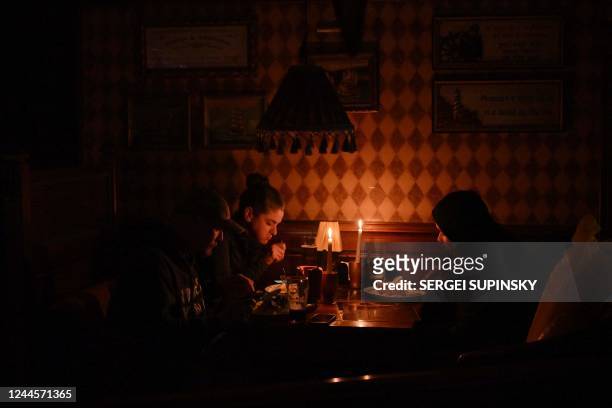 This photograph taken on October 24 shows visitors eating lunch by candlelight due to a power cut at a bar in the center of Ukrainian capital of...