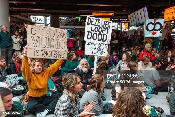 Activists hold placards during a non-violent sit-in demonstration at the Shopping Plaza of Schiphol Airport. More than 200 Extinction Rebellion and...