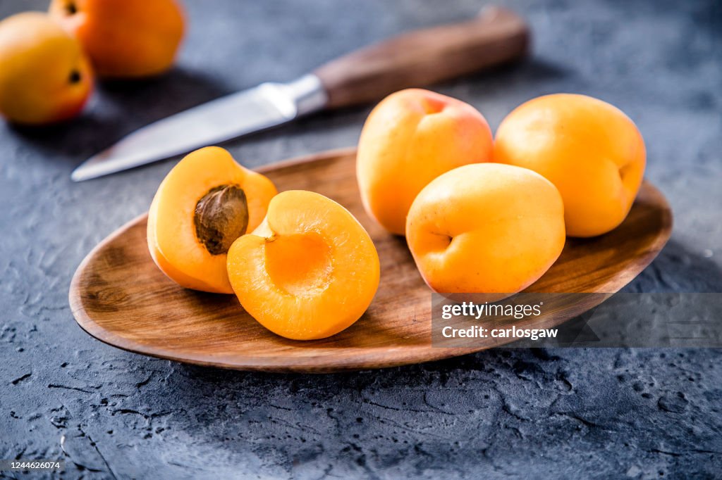 Whole and sliced apricots with a kitchen knife on a gray bluish backdrop