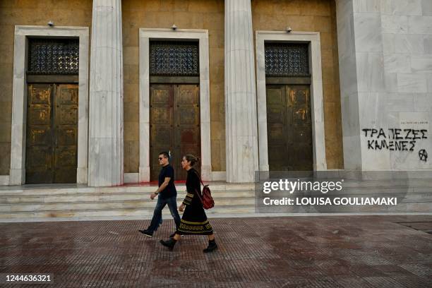 Pedestrians walk past a graffiti reading "banks burnt" on the Bank of Greece's wall during a 24-hours general strike called by unions and private...