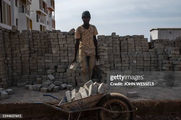Construction worker carries bricks in Diamniadio on November 8, 2022. - Littered with unfinished and finished buildings, the new city of Diamniadio...