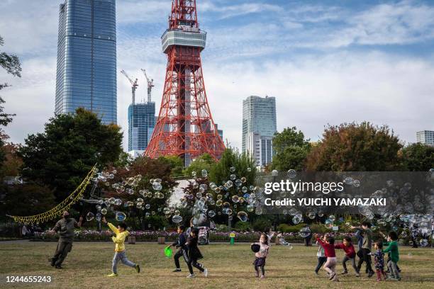 Children play with bubbles as the Tokyo tower looms in the background in Tokyo on November 10, 2022.