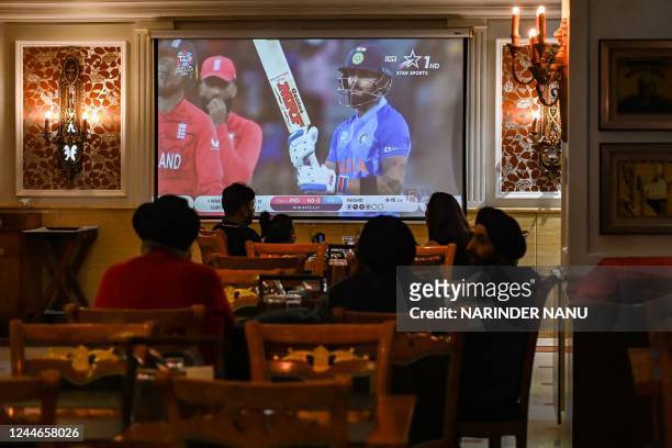 People watch the ICC men's Twenty20 World Cup 2022 semi-final cricket match between India and England in Australia, being aired on a television set...