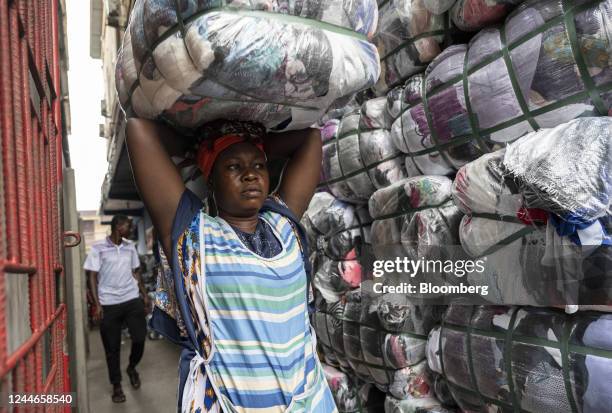 Female porter, known as 'kayayei', carries a bale of second-hand garments on her head at the Kantamanto textile market in Accra, Ghana, on Thursday,...