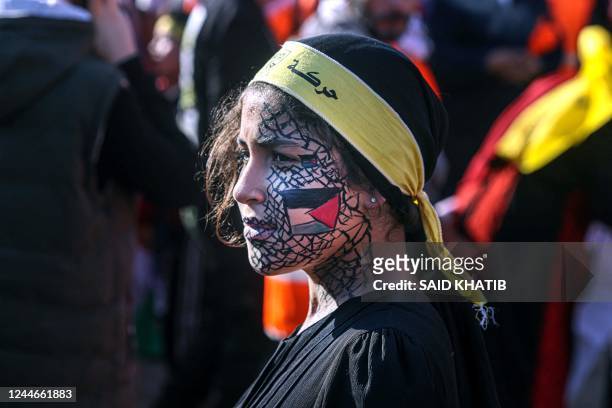 Girl with face-paint depicting the Palestinian flag looks on as others gather with flags of the Fatah movement during a rally commemorating the 18th...