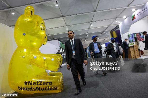 Delegates walk past an inflatable bear showing English text "#NetZero Needs Nuclear" outside the St Kitts and Nevis pavilion at the Sharm el-Sheikh...