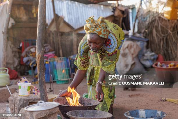 Woman lights a fire outside a makeshift shelter at the Faladie internally displaced people camp in Bamako on November 9, 2022. - People fleeing a...