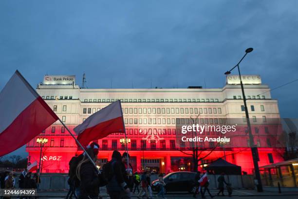 People walk past of a building lighted in white and red, during the Independence day march organized on the 104th Anniversary of regaining...