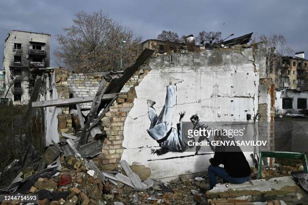 Local resident looks at a Banksy-style graffiti on the wall of a destroyed building, but its origin remains unconfirmed by the artist, in Borodyanka,...