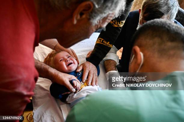 Members of the Muslim community comfort a child while a doctor performs a circumcision during a circumcision ceremony for young boys in the village...