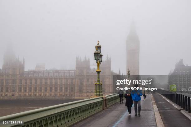 People walk along Westminster Bridge past the Houses of Parliament and Big Ben as thick fog covers the capital.