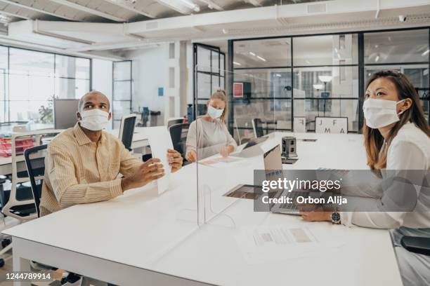 geschäftsleute, die im büro mit glastrennwand arbeiten, die sie teilen - occupational safety and health stock-fotos und bilder