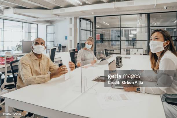 businesspeople working at office with glass partition dividing them - social distancing stock pictures, royalty-free photos & images