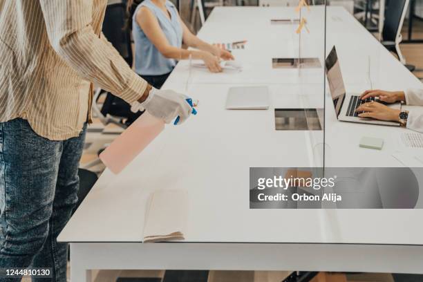 man in the office using disinfectant for sanitizing monitor surface during covid-19 pandemic - corporate business covid stock pictures, royalty-free photos & images