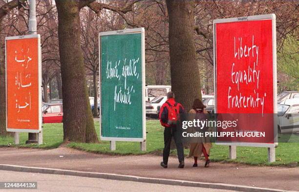 Un homme et une femme passent devant des panneaux sur lesquels des affiches portant la mention "Liberté, Egalité, Fraternité" en langue arabe,...