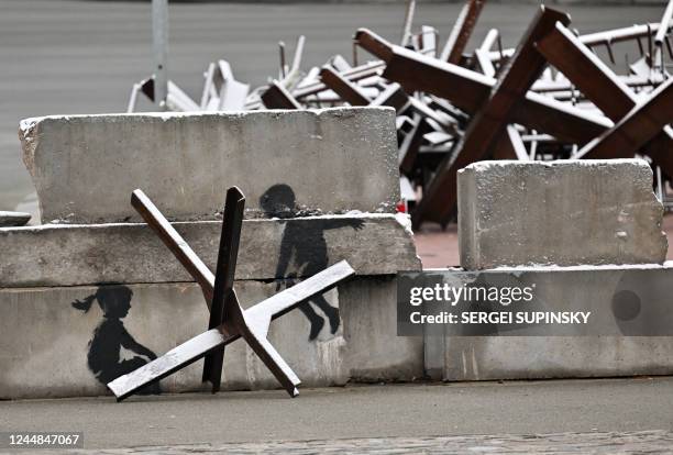 This photograph taken on November 17 shows a piece by British street artist Banksy on an anti-tank constructions covered with snow, after the first...