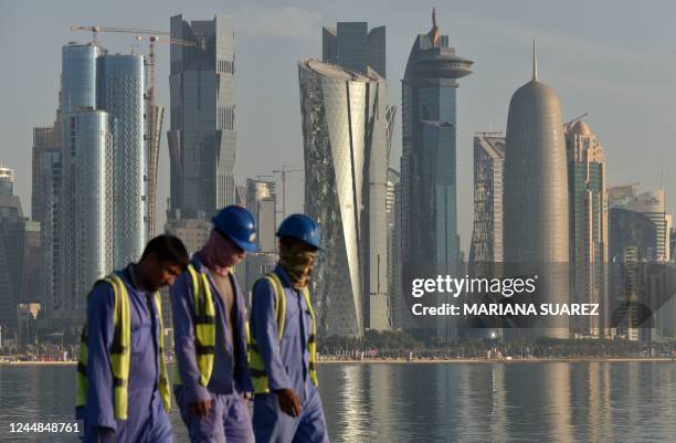 Workers are backdropped by the skyline of Doha as they walk along the Corniche seafront promenade in Doha early morning on November 17 ahead of the...