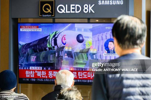 People sit near a television showing a news broadcast with a file photo of a North Korean intercontinental ballistic missile on display during a...