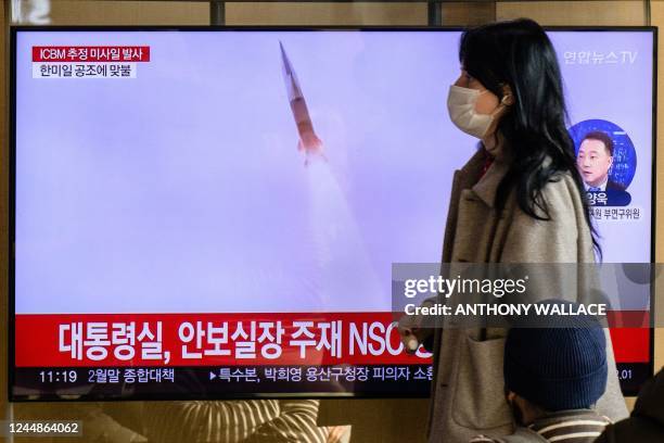 Woman walks past a television showing a news broadcast with file footage of a North Korean missile test, at a railway station in Seoul on November...