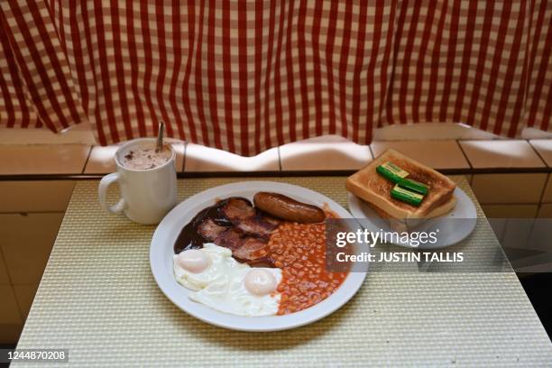 Full English breakfast with eggs, baked beans, bacon, sausage and gravy sauce is served on a table alongside a cup of coffee and bread with butter at...