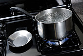 Pot of water boiling on a black natural gas stove.