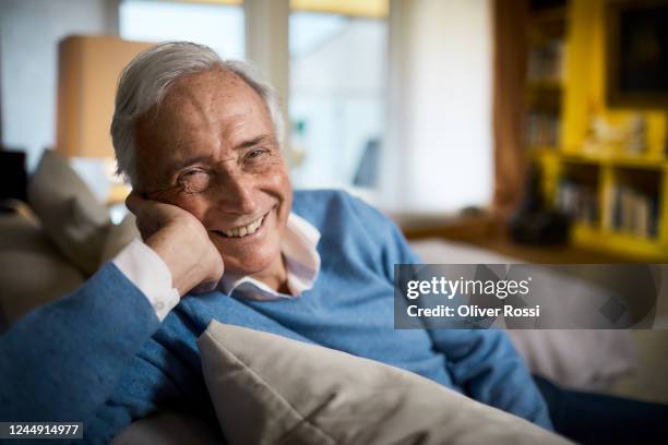 portrait of happy senior man sitting on couch at home - happy retirement stock-fotos und bilder