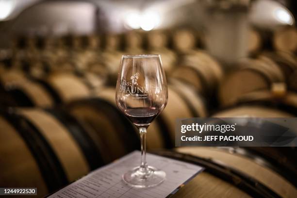 This photograph taken on November 20 shows a glass of wine and a notebook on a wine barrel in the "Nouvelle cuverie" of a wine that will be sold...