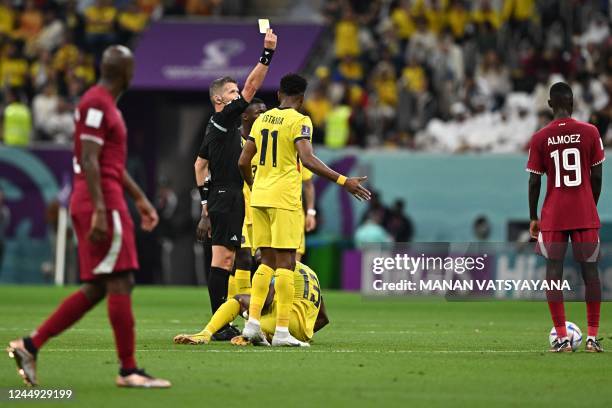 Italian referee Daniele Orsato issues a yellow card to Qatar's midfielder Karim Boudiaf after he tackled Ecuador's forward Enner Valencia during the...