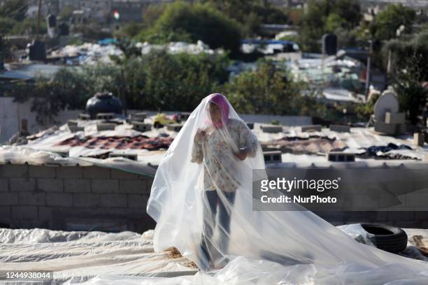 Palestinian girl lays a sheet of plastic to cover the roof of a shack from the effects of bad weather in Gaza City on November 20, 2022.