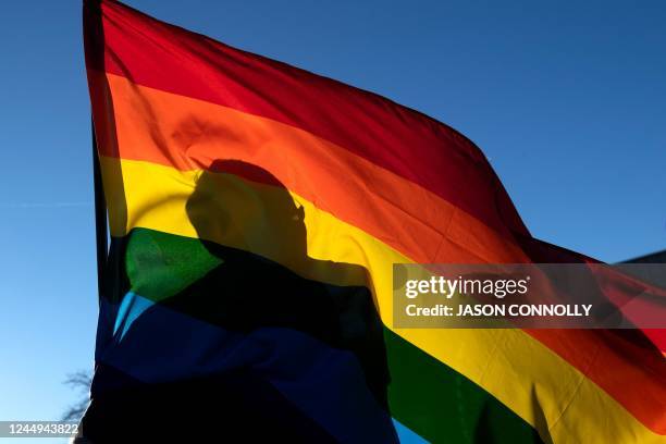 Commuity member's silhouette is seen through a Pride flag while paying their respects to the victims of the mass shooting at Club Q, an LGBTQ...