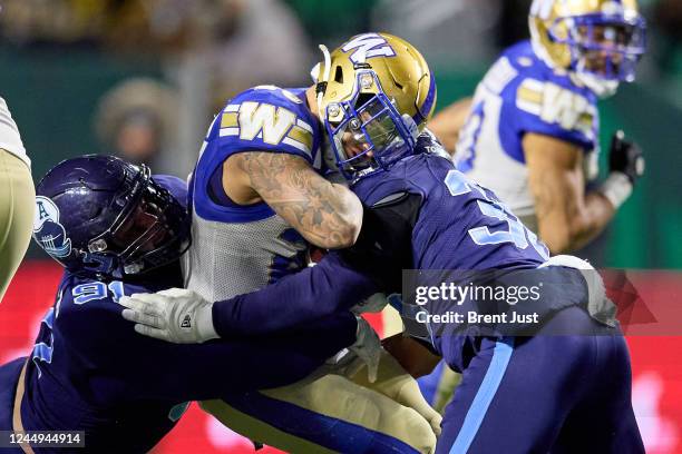 Brady Oliveira of the Winnipeg Blue Bombers is sandwiched on a tackle by Jonathan Jones and Jared Brinkman of the Toronto Argonauts in the first half...