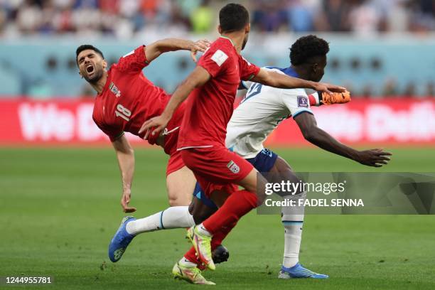 Iran's midfielder Ali Karimi reacts as he fights for the ball with England's forward Bukayo Saka during the Qatar 2022 World Cup Group B football...