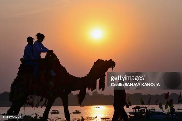 People ride a camel as they are silhouetted against the setting sun at Sangam, the confluence of the rivers Ganges, Yamuna, and mythical Saraswati,...