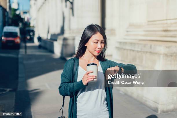 confident young woman checking time on her watch while commuting to work with coffee - watch time stock pictures, royalty-free photos & images