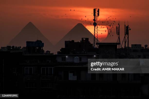 Flocks of pigeons fly as the sun sets behind the Great Pyramid of Khufu , the Pyramid of Khafre , and the skyline of Giza, the twin city of Egypt's...