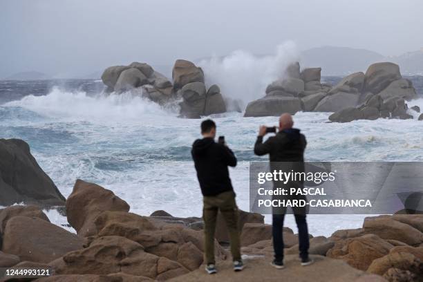 Picture taken on November 22, 2022 from Albitreccia shows men taking pictures of big waves breaking on the Sette Nave rocks as storm Denise hits the...