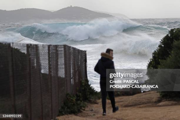 Picture taken on November 22, 2022 from Albitreccia shows a man walking as big waves break onshore as storm Denise hits the French Mediterranean...