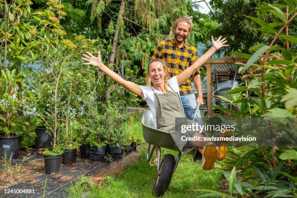 junges paar spielt im garten mit schubkarre - wheelbarrow stock-fotos und bilder