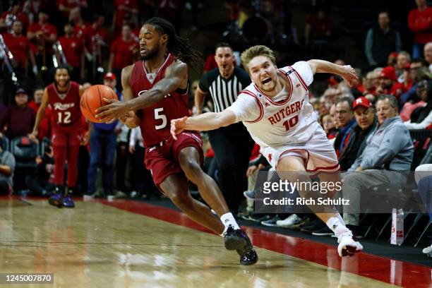 Cam Spencer of the Rutgers Scarlet Knights attempts to steal the ball away from Mervin James of the Rider Broncs during the second half of a game at...