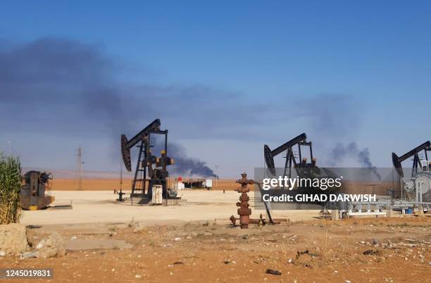This picture shows pumpjacks in an oil field and smoke plumes rising in the background, following reported Turkish drone strikes near the town of...