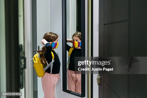 Young girl putting on her face mask in mirror by front door Young girl putting on her face mask in mirror by front door