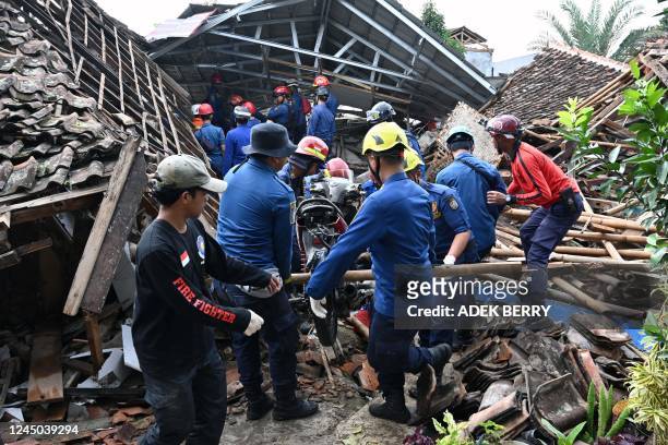 Rescue personnel remove a motorcyle as they work to find a missing child believed to be trapped in the rubble of a collapsed house at Cugenang in...