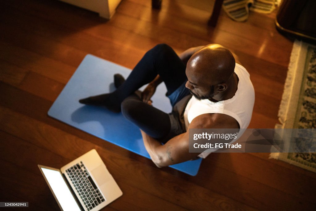 Man watching gym class on laptop and doing exercises at home