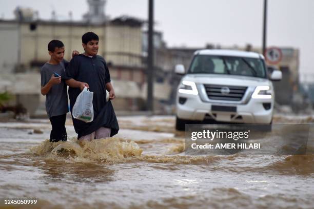 Youthd walk in a flooded street following heavy rains in the Saudi coastal city of Jeddah on November 24, 2022 which delayed flights, forced school...