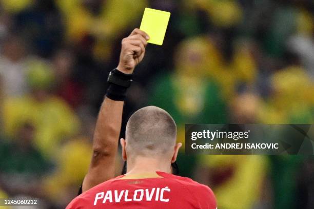 Iranian referee Alireza Faghani shows a yellow card to Serbia's defender Strahinja Pavlovic during the Qatar 2022 World Cup Group G football match...