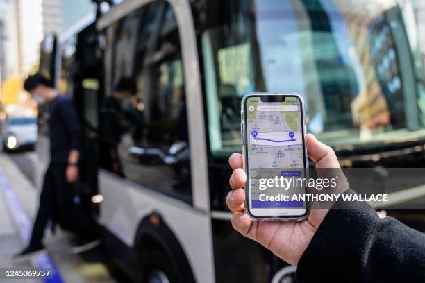 This photo taken in Seoul on November 23, 2022 shows a person posing with a phone to show the app for the country's first self-driving bus route run...