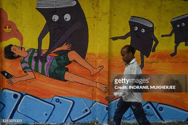 Man walks past a satirical wall mural portraying a teenager affected by social media addiction, in Mumbai on November 25, 2022.